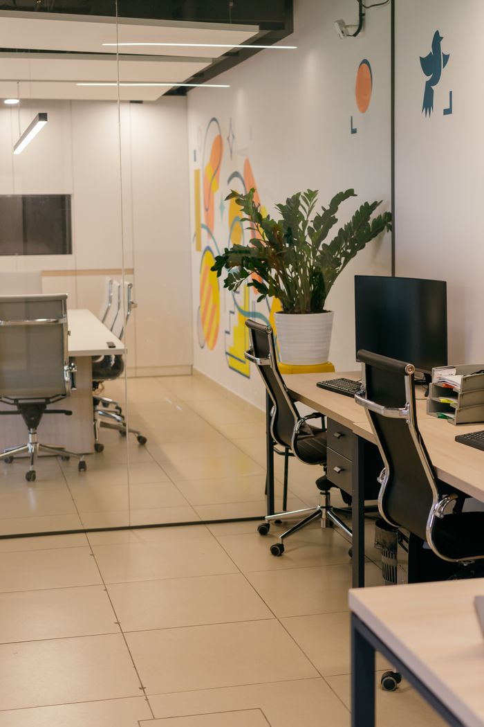 Interior de bureau spacieux et moderne avec des cloisons vitrées, du mobilier élégant et des œuvres murales aux couleurs vives.